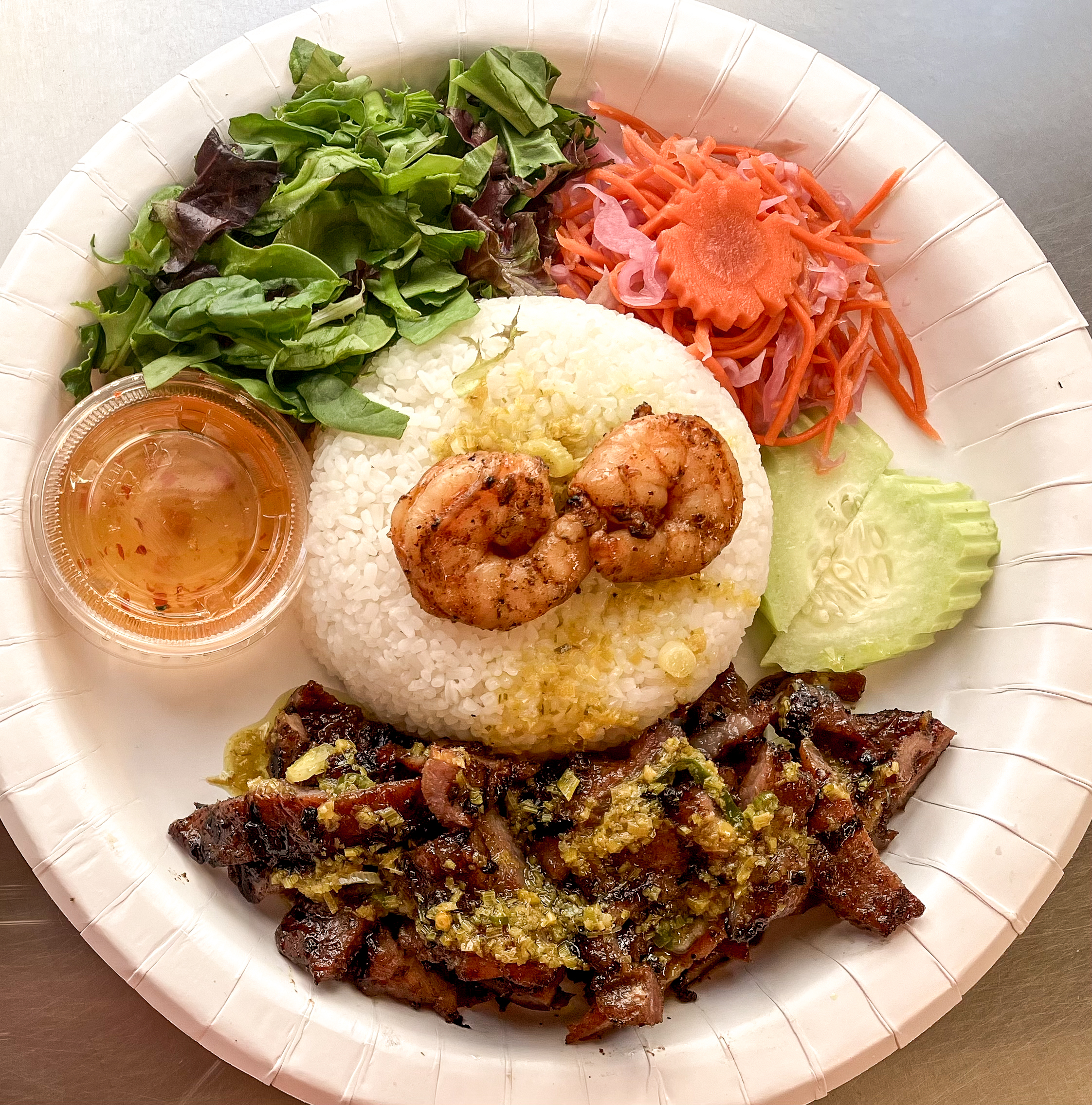 Broken jasmine rice plate with grilled shrimp, grilled pork, fresh salad, pickled carrots, cucumber slices, and a cup of fish sauce