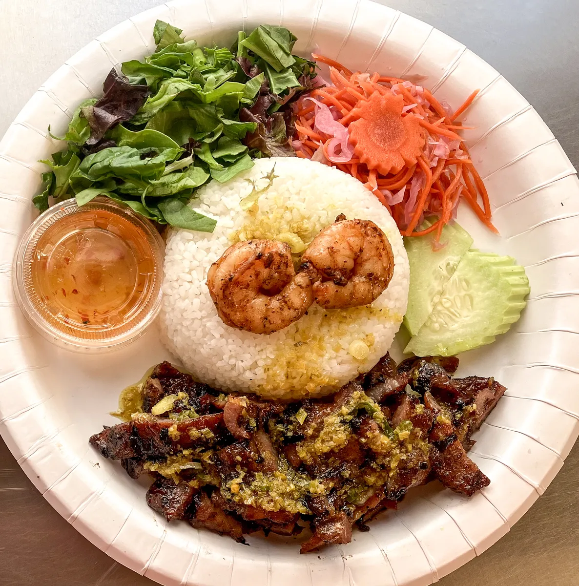 Broken jasmine rice plate with grilled shrimp, grilled pork, fresh salad, pickled carrots, cucumber slices, and a cup of fish sauce